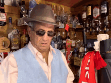 a man wearing a hat and sunglasses stands in front of a shelf full of liquor including a bottle of lemoncello