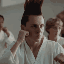 a young man with a mohawk is wearing a white karate uniform and making a fist .