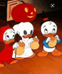 three cartoon ducks dressed in halloween costumes are standing next to a pumpkin .