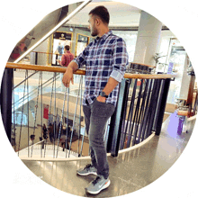 a man in a plaid shirt leans on a railing in front of a store called kings