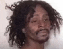 a man with curly hair and a beard is looking at the camera with his eyes closed .