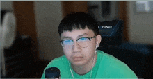 a young man wearing glasses and ear buds is sitting in front of a computer screen .