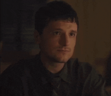 a man in a suit and tie is sitting at a table in a dark room and looking at the camera .