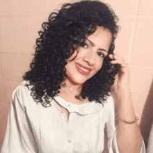 a woman with curly hair wearing a white shirt smiles for the camera