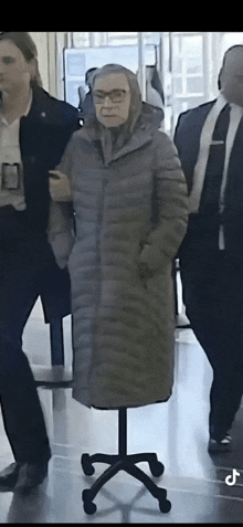 a woman in a coat and scarf stands on a chair