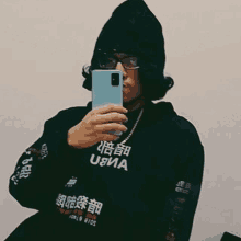 a man is taking a selfie with his cell phone while wearing a beanie and glasses .