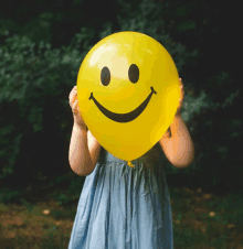 a girl in a blue dress holds a yellow balloon with a smiley face on it