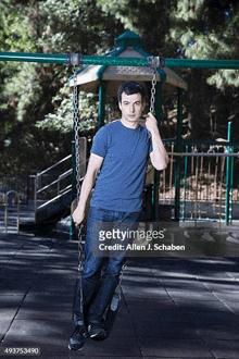 a young man is standing on a swing in a park