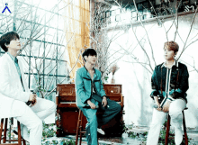 three men are sitting on stools in front of a piano in a room with trees