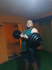 a man in a green tank top is lifting a barbell in a dark room