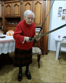 an elderly woman in a red coat holds a sword