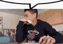 a young man wearing a miami heat sweatshirt covering his nose