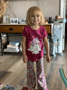 a little girl wearing a pink unicorn shirt and floral pants