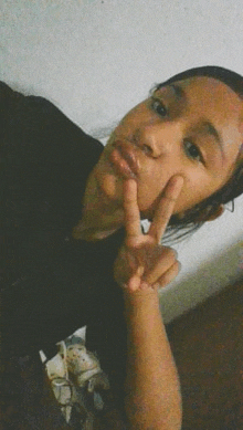 a young girl is taking a selfie and making a peace sign with her fingers .