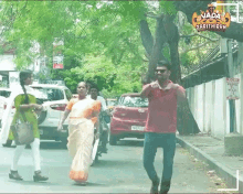 a man in a red shirt is walking down a street next to a woman in a white saree .