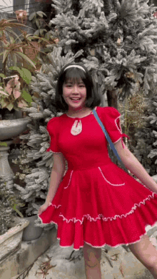 a girl in a red dress is standing in front of a snowy christmas tree