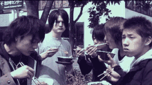 a group of young men are eating food with chopsticks in front of a building with a sign that says outdoor center