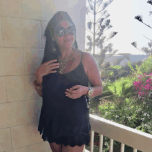 a woman wearing sunglasses and a black tank top stands on a balcony