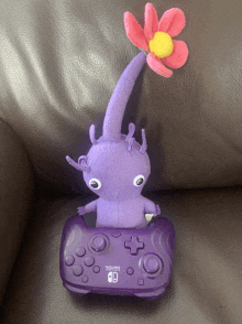 a purple stuffed animal is sitting on top of a purple nintendo switch controller