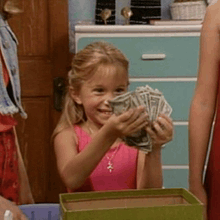 a little girl in a pink tank top is holding a bunch of money in her hands