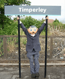 a man in a suit holds up a sign for timperley