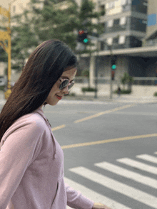 a woman wearing sunglasses and a pink hoodie is crossing the street