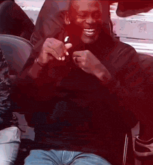 a man wearing a black shirt and blue jeans is sitting in a chair and smiling