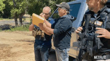 a man holding a gun stands next to two other men with netflix written on the bottom of the image