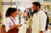 a man and a woman are standing next to each other in a mall and the woman is looking at her phone .