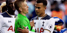 two soccer players are standing next to each other and one of them is wearing a green jersey with the letter a on it .