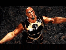 a bald man with a beard is standing in the dirt with his arms outstretched in a video game .