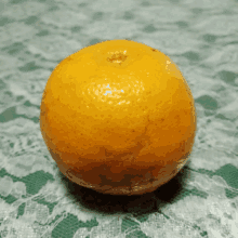 an orange sits on a green and white lace tablecloth