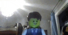 a green lego man is sitting in a room with a laptop on his back .