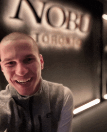 a man smiles in front of a sign that says " nobu toronto "