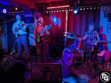 a group of men are playing instruments on a stage with a n on the bottom right