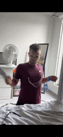 a man in a maroon nike shirt is standing in a bedroom holding a knife .