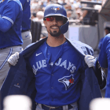 a man wearing a blue jays jersey is taking off his jacket