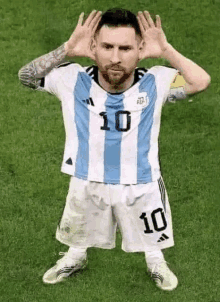 a soccer player wearing a blue and white striped jersey is standing on a field with his hands on his head .