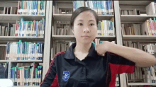 a woman wearing a black and red shirt with a blue emblem on it is standing in front of a bookshelf in a library