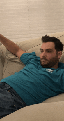 a man laying on a couch with his arms outstretched wearing a teal shirt that says samsung on it