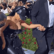 a woman in a black dress is holding the hand of a man in a tuxedo at a red carpet event .