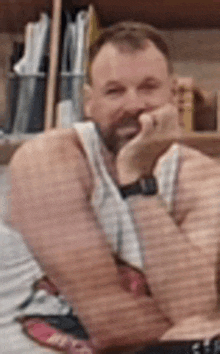 a shirtless man with a beard is sitting on a bed with his arms crossed and his hand on his chin .