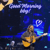 a man singing into a microphone while playing a guitar with the words " good morning bby " written above him