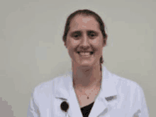 a woman is wearing a white lab coat and smiling for the camera .