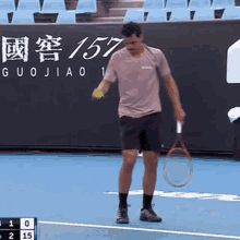 a man is holding a tennis racquet and a tennis ball on a tennis court with 157 written on the wall behind him