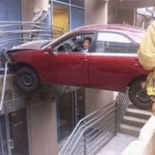 a red car is stuck in a building next to stairs .