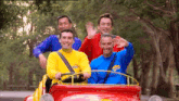 a group of men wearing wiggle shirts are driving a red car