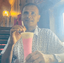 a man sitting at a table drinking a pink milkshake