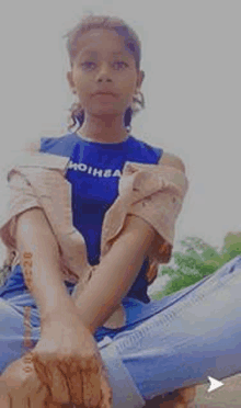 a young girl is sitting on the ground with her legs crossed and looking at the camera .