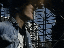 a man in a denim shirt is standing in front of a scaffolding structure with a sign that says ' this '